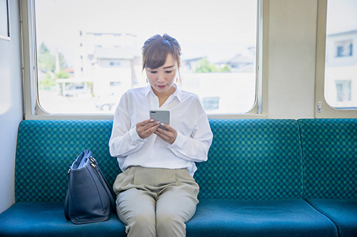 「電車の座席に座ってスマホを見る女性」の写真
